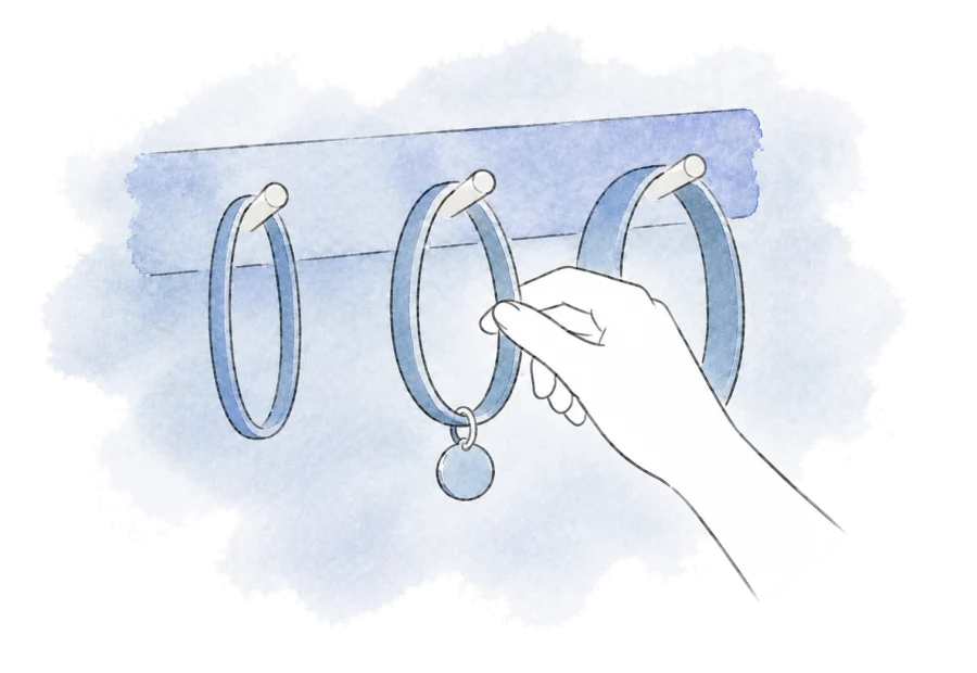 A hand selects one collar from a few hanging on hooks.