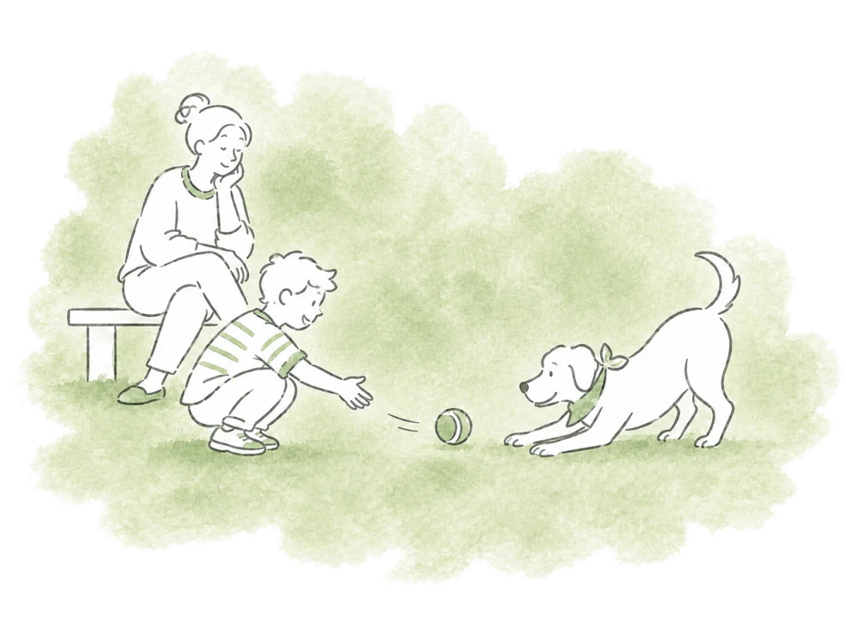 A child rolls a ball to a playful dog beside an adult.