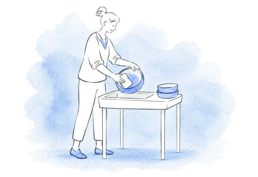 A volunteer washes a feeding bowl beside the clean bowls from the daily round.